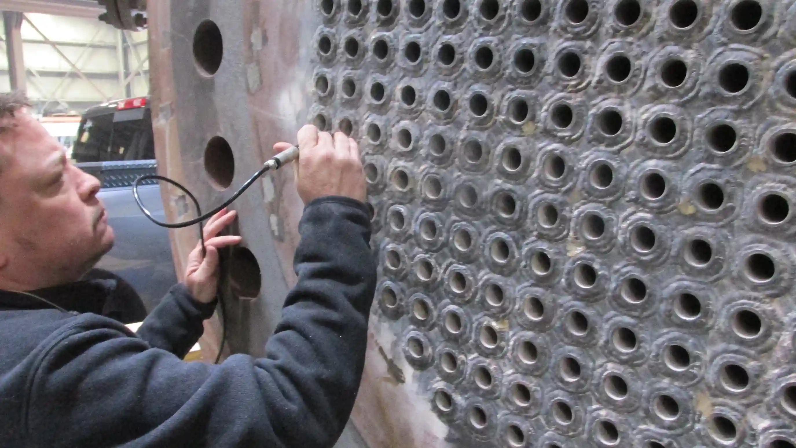 Technician using an inspection probe to check heat exchanger tube sheet openings for damage or wear.