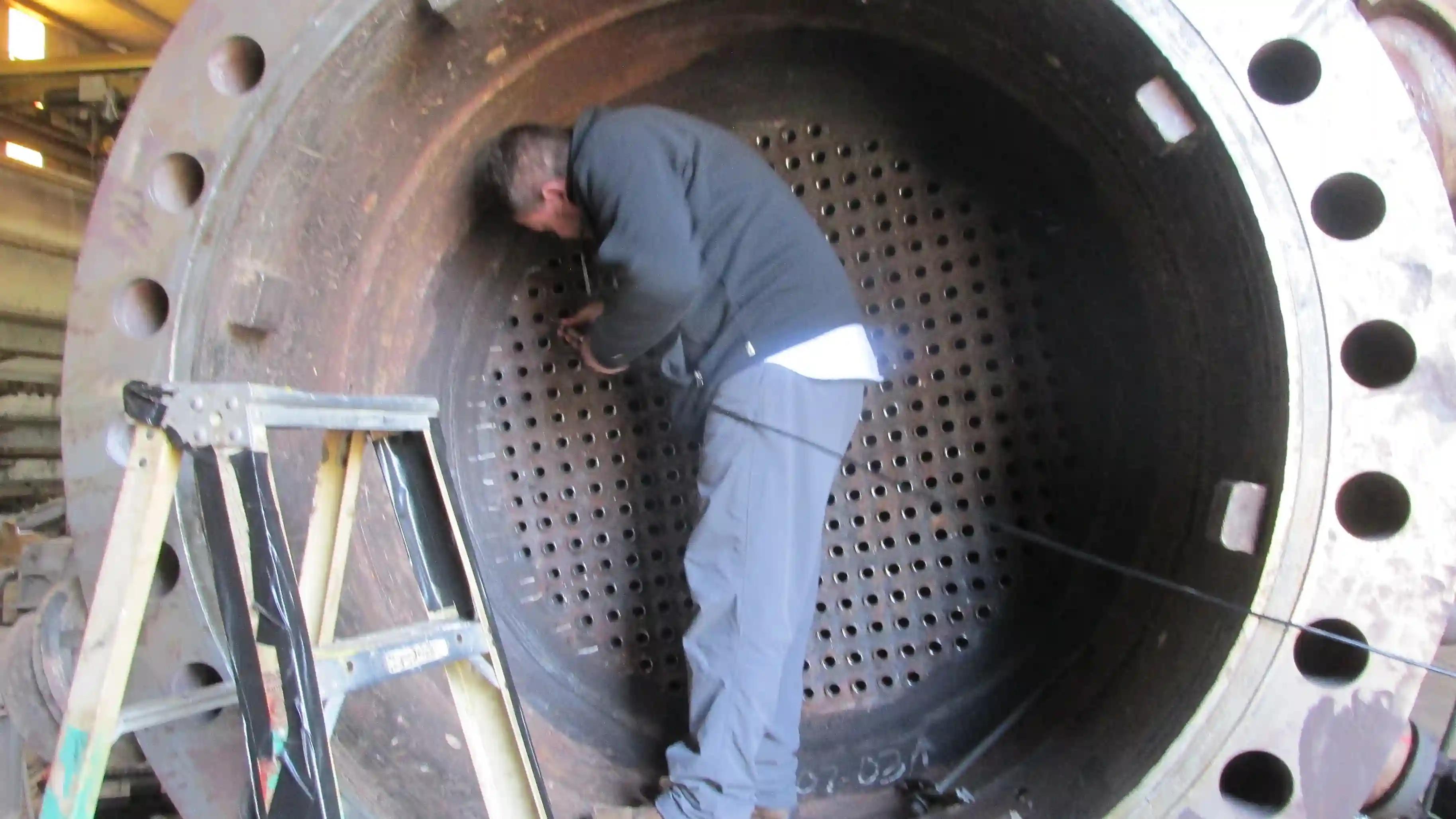 Technician inspecting the inside of a heat exchanger tube sheet for condition and integrity checks.