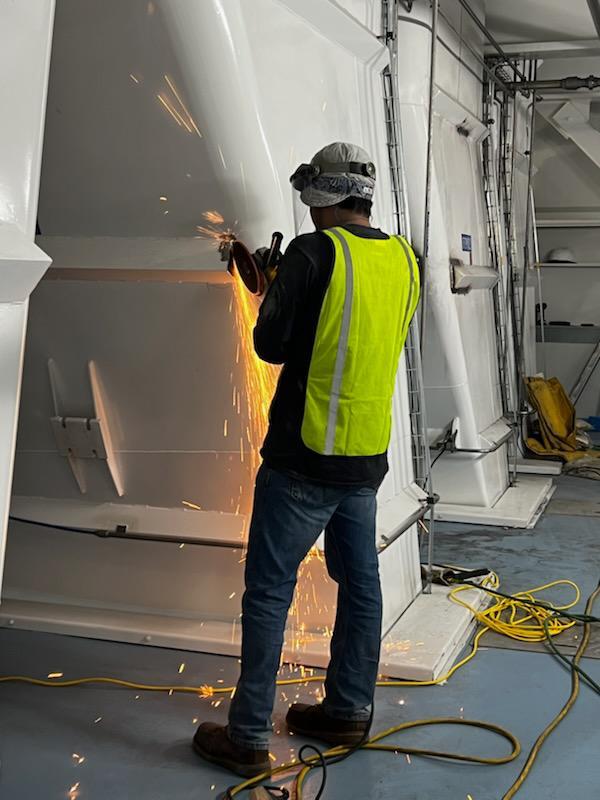 Technician grinding a metal surface to prepare for NDT visual inspection.